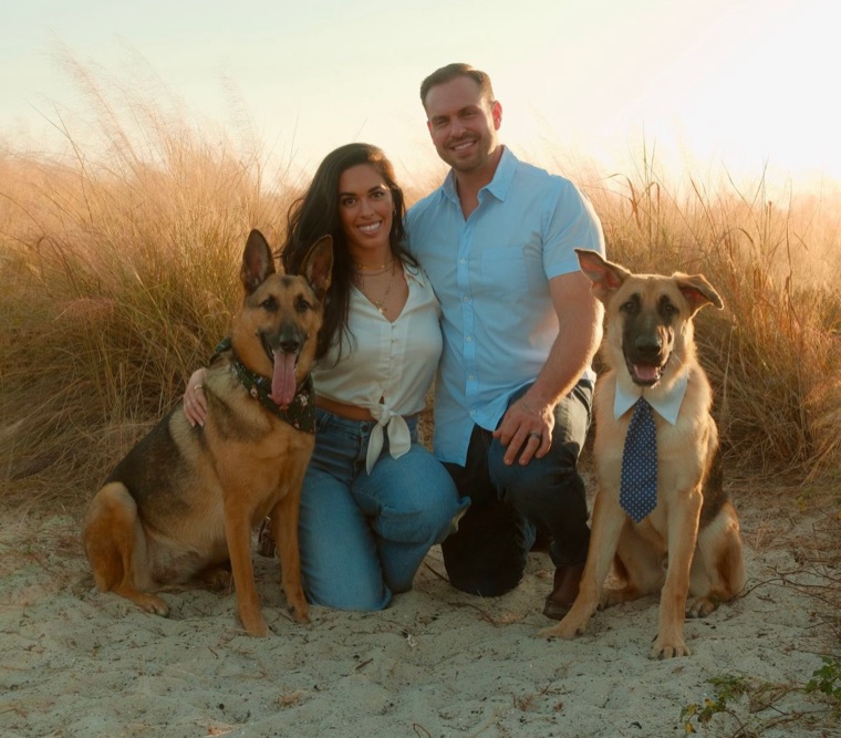Ryan Caprio and his wife kneeling in the sand with their two German shepherds, one in a bandana and one in a tie